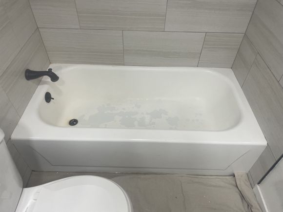 Dingy bathtub in a modern gray-tile bathroom before refinishing